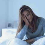 Woman sitting in bed with hand on face, looking tired