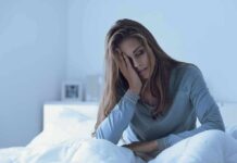 Sleeping More, Still Exhausted? Here’s Why Woman sitting in bed with hand on face, looking tired
