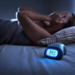 Person lying awake in bed beside a glowing digital alarm clock