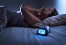 Body Clock Rhythm and Dementia Risk Person lying awake in bed beside a glowing digital alarm clock