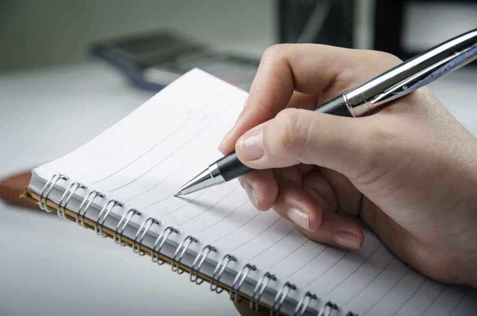 shutterstock_131199218 A hand holding a pen above a blank notebook page
