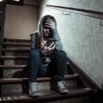 teen girl sitting on stairs looking at phone with hand on forehead