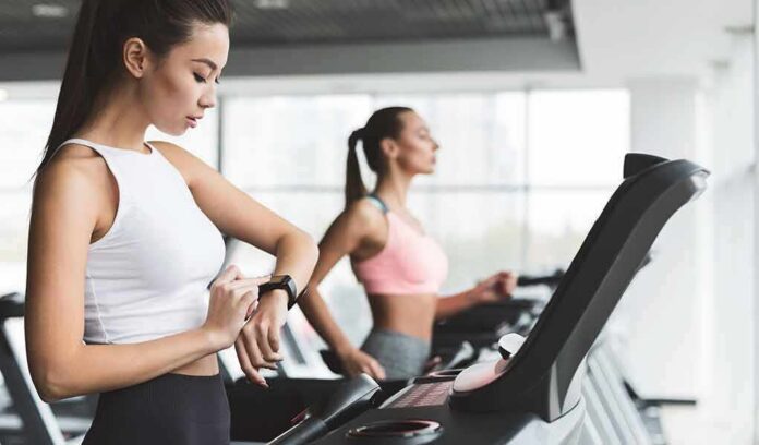 Woman on treadmill checking smartwatch in gym
