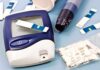 Blood glucose monitor with testing strips and a lancing device on a blue background