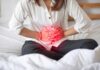 The Constipation Line You Mustn’t Cross Woman holding her abdomen in pain while sitting on a bed