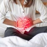 Woman holding her abdomen in pain while sitting on a bed