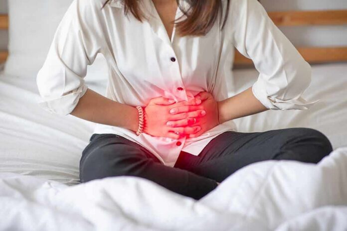 Woman holding her abdomen in pain while sitting on a bed