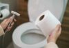 Hands holding a bidet sprayer and toilet paper near an open toilet