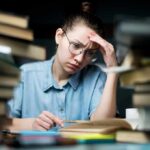 Student with glasses studying amid stacks of books