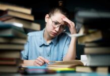 Student with glasses studying amid stacks of books