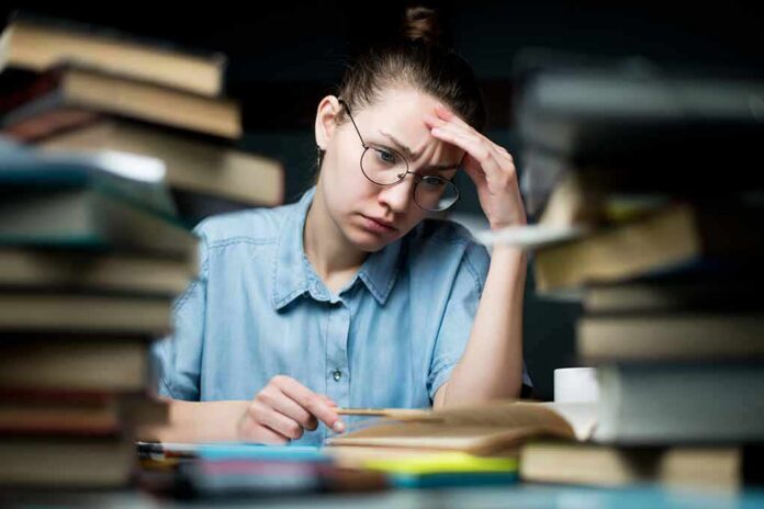 Student with glasses studying amid stacks of books