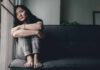 Health Risks of Isolation and Loneliness Woman sitting on a couch hugging her knees by a window