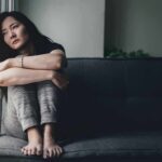 Woman sitting on a couch hugging her knees by a window