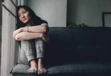 Woman sitting on a couch hugging her knees by a window