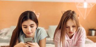 Two girls lying on a bed using smartphones