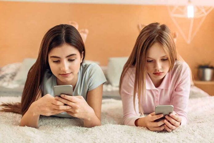 shutterstock_1015950148 Two girls lying on a bed using smartphones