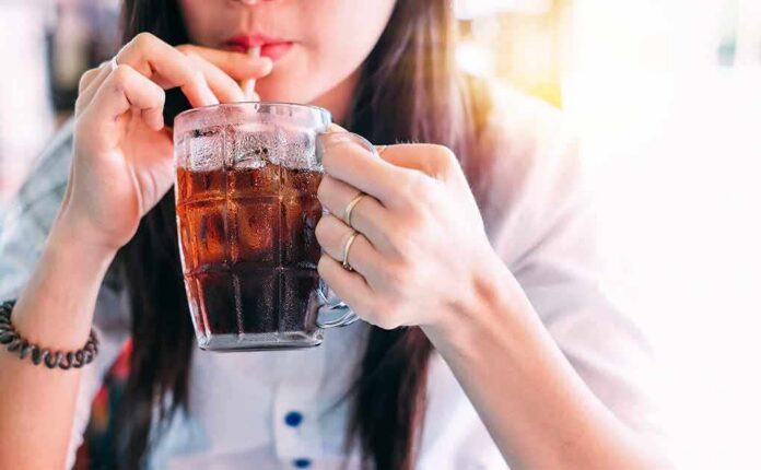 shutterstock_1033381774 person sipping iced drink from a glass mug with a straw