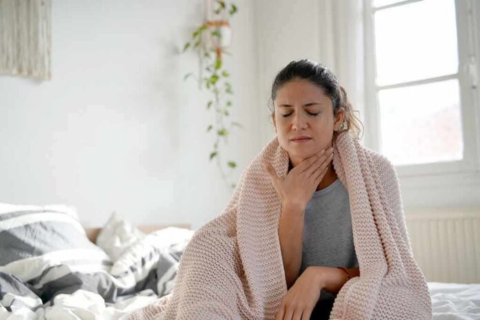 shutterstock_1257992872 Woman wrapped in blanket touching her throat