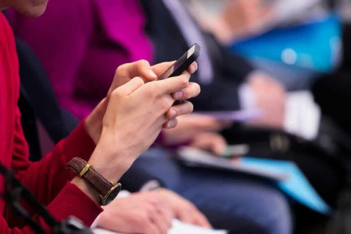 shutterstock_1350965177 Person in red sweater using a smartphone at an event