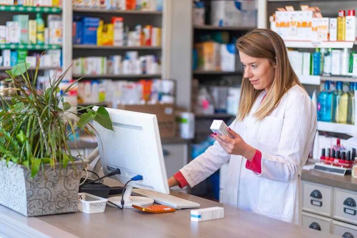 shutterstock_1385081492 Pharmacist checking medication box at computer counter