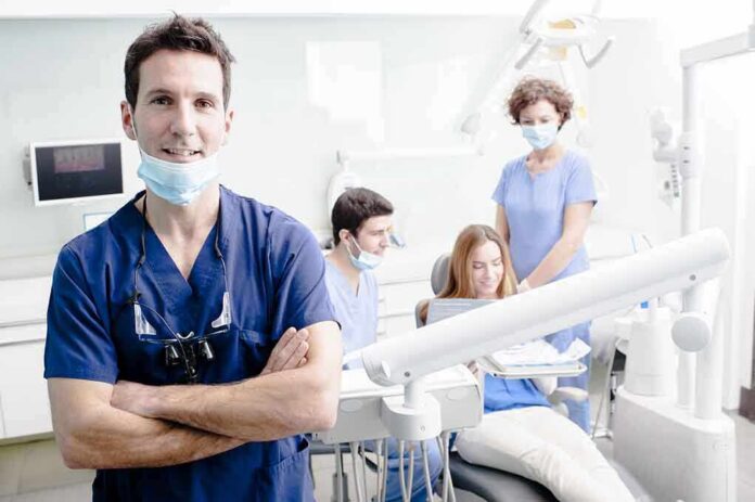 Dentist in scrubs stands with arms crossed in a bright dental clinic
