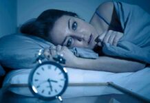 The Sleep Trick That Finally Turns Your Brain Off Woman lying awake in bed beside an alarm clock