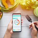 hands holding phone with calorie tracker beside salad and pastry