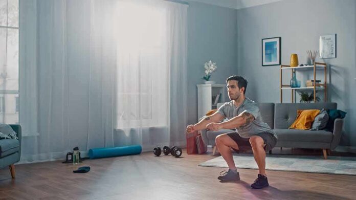 shutterstock_1497529373 Man doing bodyweight squats in a living room