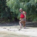 man in red life vest walking through muddy riverbank