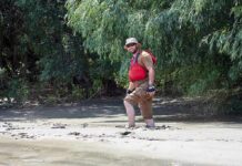 man in red life vest walking through muddy riverbank