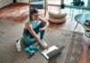 Woman in workout clothes using a laptop on a living room rug