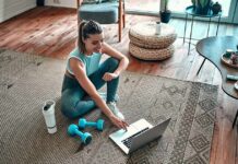 Woman in workout clothes using a laptop on a living room rug