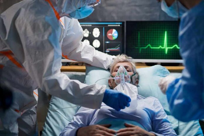 shutterstock_1661222104 Patient on hospital bed with oxygen mask and medical staff in protective gear