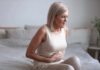 Chronic Pain Management – A Patient’s Guide Older woman sitting on bed holding her stomach in pain