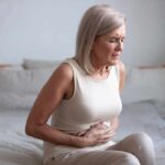 Older woman sitting on bed holding her stomach in pain