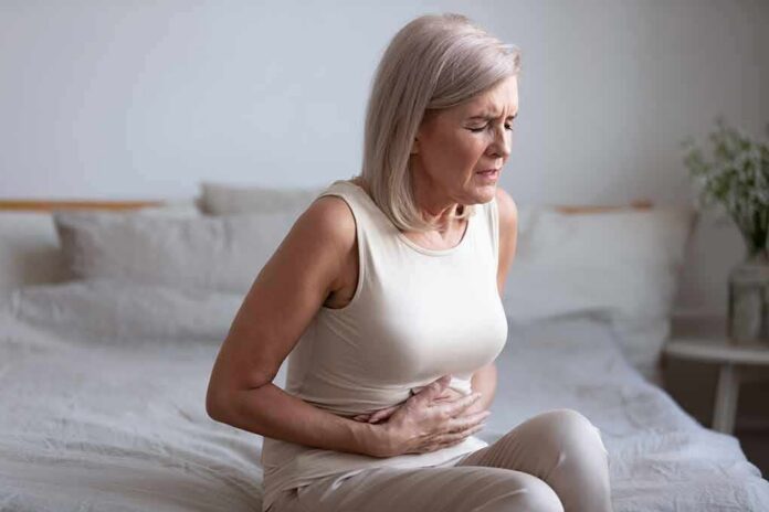 Older woman sitting on bed holding her stomach in pain