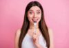 Woman holding a fork to her teeth against a pink background