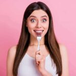 Woman holding a fork to her teeth against a pink background