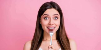 Woman holding a fork to her teeth against a pink background