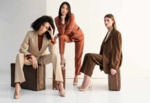 Three women in tailored suits posing on vintage suitcases