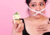 Woman with measuring tape over mouth holding a decorated cupcake
