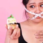 Woman with measuring tape over mouth holding a decorated cupcake