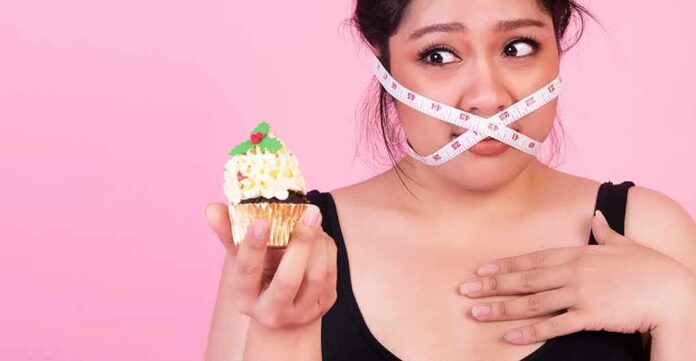 Woman with measuring tape over mouth holding a decorated cupcake