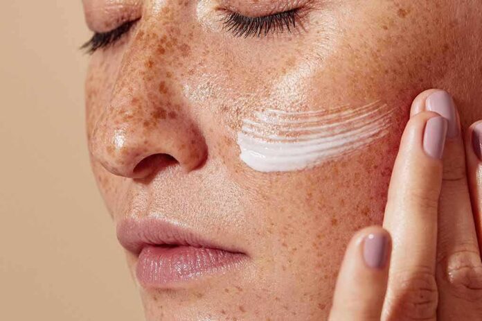 Close-up of face with freckles applying cream to cheek