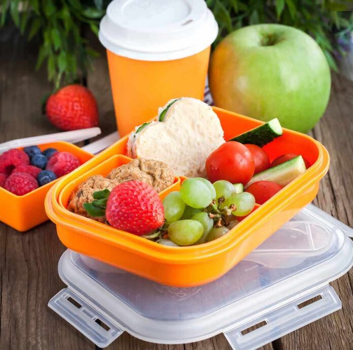 Orange lunchbox with fruits, veggies, cookies, and a small sandwich
