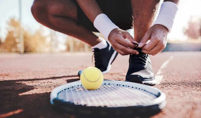 shutterstock_697394095 Tennis player tying shoelaces on a clay court