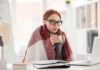 Woman in glasses wrapped in a blanket holding a mug at a laptop