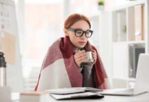 WHO Flags ‘Very Hot’ Drinks Woman in glasses wrapped in a blanket holding a mug at a laptop