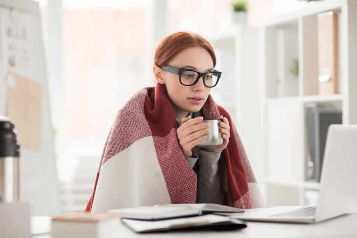 shutterstock_790118056 Woman in glasses wrapped in a blanket holding a mug at a laptop