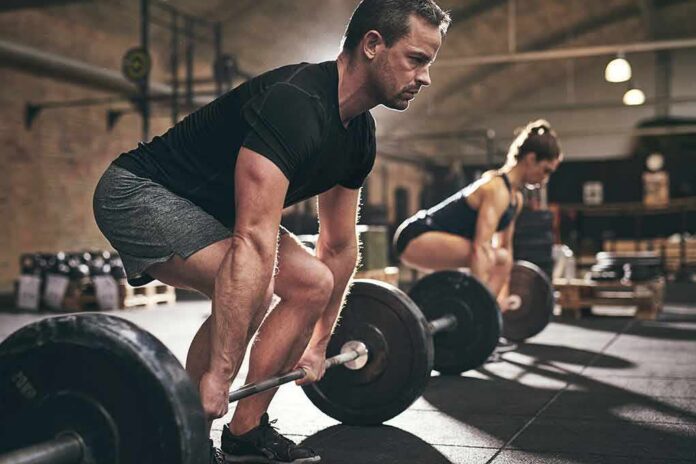 Two people performing deadlifts in a gym